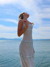Woman in a white dress standing by the water with a blue sky background